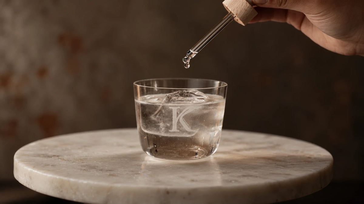 Pipette über einem Glas mit K-Monogramm auf einem Marmortisch